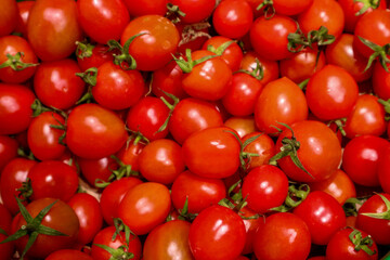 Cherry tomatoes in a plastic box in the store. Fresh shiny cherry tomatoes sitting in a larger straw basket of small tomatoes. Basket of organic tomatoes is sitting on a grocery shelf in a store.