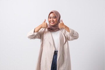 Portrait of attractive Asian hijab woman in casual suit making thumb up hand gesture, saying good...