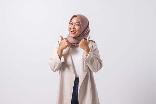 Portrait of attractive Asian hijab woman in casual suit making thumb up hand gesture, saying good job. Businesswoman concept. Isolated image on white background
