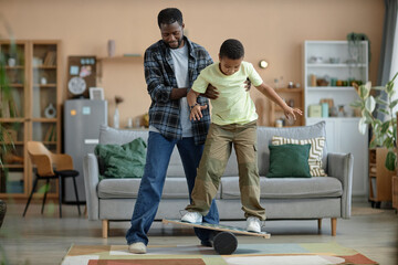Full length portrait of African American father teaching son standing on balance board - 772912542