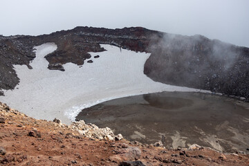 View of the volcano crater. Mountain landscape. Snow and lake in a volcanic crater. Travel and hiking on the Kamchatka Peninsula. Nature of the Russian Far East. Gorely volcano, Kamchatka Krai, Russia - 772913947