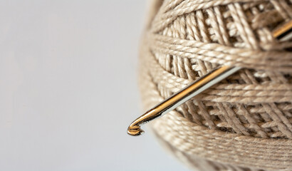 Close-up on a skein of natural beige cotton yarn and a metal crochet hook. Empty space for text on the left on a white background. DIY concept. Flat lay, copy space, macro