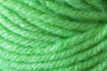 Close-up of a skein of natural woolen green yarn for hand knitting or crocheting. The texture of wool threads wound into a ball. Textile background. Flat lay, macro, top view, copy space