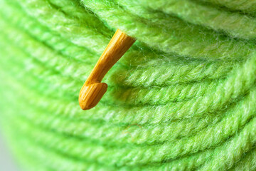 Close-up of a skein of green wool soft yarn and a wooden crochet hook. The texture of woolen threads wound into a ball. Textile background. DIY concept. Flat lay, macro, top view