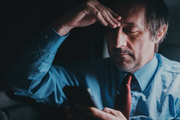Businessman using cell phone at the back seat of the car will traveling home from the work late at night, low key