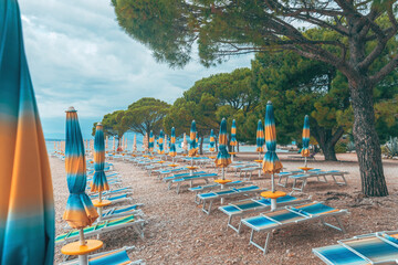 Obraz na płótnie Canvas Folded beach umbrellas and empty deck chairs on town beach in Crikvenica, Croatia. Overcast weather and cloudy days during poor touristic season.