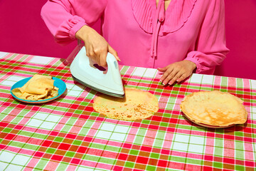 Woman in pink blouse ironing pancake on plaid tablecloth. Meme featuring unexpected ways to prepare food through humor. Concept of pop art, creativity, weirdness, food, humor, colorful photography - 772922734