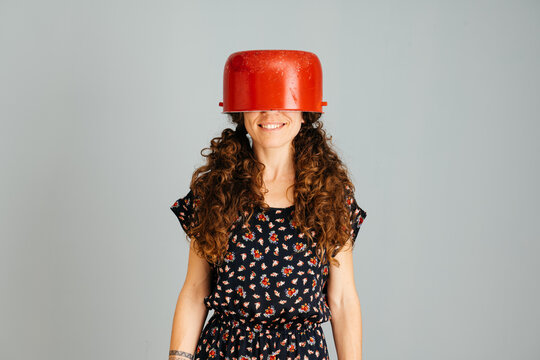Woman Smiling With Red Cooking Pot on Her Head Against a Plain Background