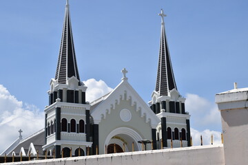 The roof of the Catholic Church behind a concrete fence against the blue sky. - Powered by Adobe