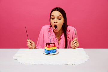 Young woman in pink shirt sitting at table with birthday cake made of dishwashing sponges, making birthday wishes and blowing candle. Concept of food pop art photography, creativity, quirky style - obrazy, fototapety, plakaty