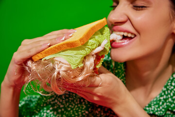 Young woman eating quirky sandwich with doll against red background. Weirdness and surrealism. Concept of food pop art photography, creativity, quirky style