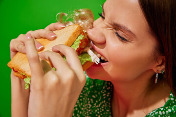 Young woman eating quirky sandwich with doll against red background. Weirdness and surrealism....