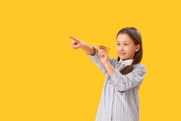 Little girl with paper plane pointing at something on yellow background. Children's Day celebration