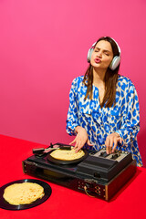Young stylish woman, dj using sound mixer with pancake instead of vinyl record on pink background. Creative music poster. Party. Concept of food pop art photography, creativity, quirky style
