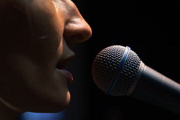 Close-up of the microphone and part of the face of a young female singer on a black background