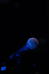 Close-up of a microphone with blue backlight in a music studio, at a concert in the dark, copy space. Vertical photo
