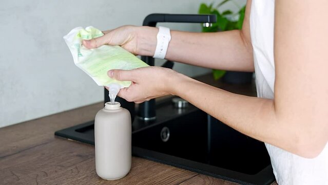 Woman pours soap or detergent from the recycled packaging into a reusable bottle. Eco-friendly lifestyle concept