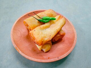 risol, traditional Indonesian food made from chicken and vegetables wrapped in flour dough served on a wooden plate on a gray background. fried food. rissoles, chili on it