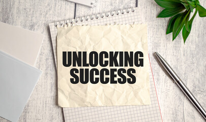 Crumpled note with UNLOCKING SUCCESS text on a textured background with pen and notepad