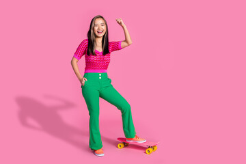 Fototapeta na wymiar Full length photo of shiny lucky lady dressed knitted shirt rising fist riding long board empty space isolated pink color background
