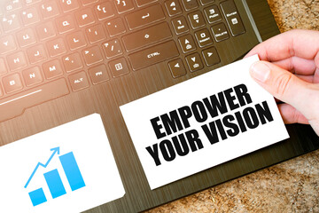 EMPOWER YOUR VISION slogan on a card held over laptop keyboard.