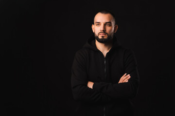 Studio shot of a serious young man with arms crossed over dark black background.
