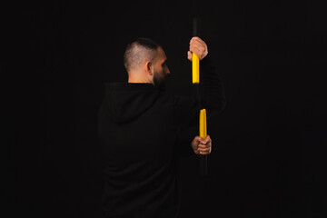 Back view studio shot of a serious young man is mastering the art of nunchaku over black background.