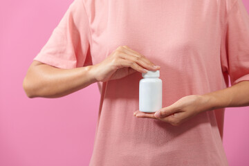 A woman hands delicately hold a bottle of medicine, isolated against pink background, depicting care, health, and the importance of pharmaceutical treatment in healthcare.