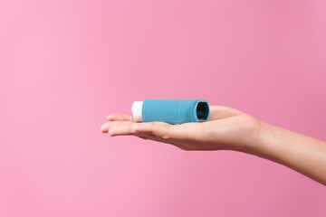 A professional image featuring a female hand holding an asthma inhaler with fingers against a soft...