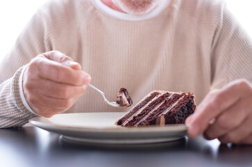 Unrecognizable elderly Caucasian man while preparing to eat a freshly baked chocolate cake, lonely...