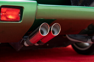 Cropped of double exhaust pipe and back part with tail light of modern green parked car. Waste...