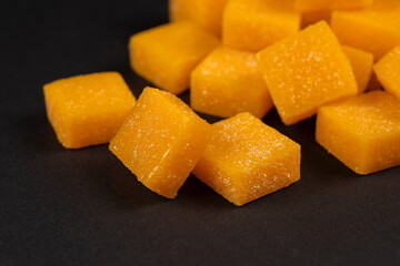 Heap of mango candy cubes on dark background.