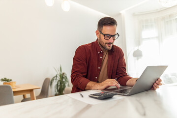 A professional adult male accountant using his laptop to read reports while working from home