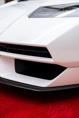 Crop of front headlight and low profile bumper of white supercar standing on red carpet....