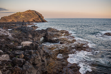 Motion of sea water in volcanic rocks at dusk with Rosto do Cão islet in background, São Miguel - Azores PORTUGAL