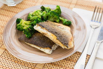 Fried fillet of sea bass with garnish of broccoli on black warm stone plate