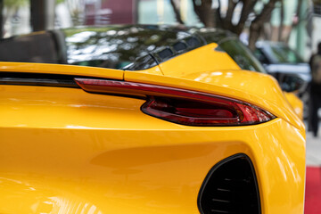 Streamlined rear bumper with elegant stop lights of expensive yellow car. Exterior surface covered...