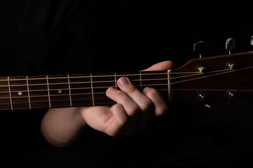 Male teenager with acoustic guitar on black background. With long hair in black clothes