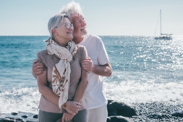 Portrait of smiling bonding senior couple in vacation standing on the seashore embrace enjoying...