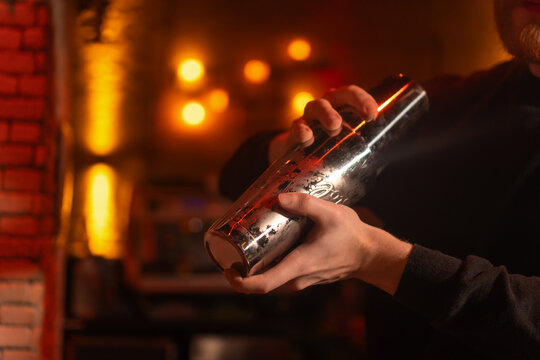 Unrecognizable male bartender mixing a drink in a cocktail shaker in a stylish modern bar.