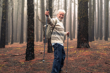 Active happy senior man with backpack walking in mountain forest on a foggy day with the help of...