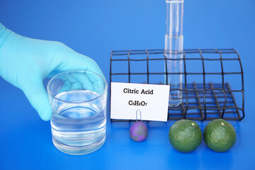 Science experiment about Citric Acid with molecular formula.C6H8O7. Hand in blue glove hold glass...