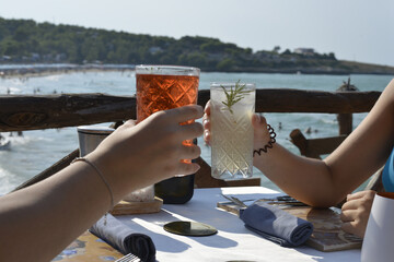 brindisi tra amici con cocktail colorati in un bar all'aperto in riva al mare - obrazy, fototapety, plakaty