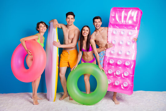 Full length photo of positive funky buddies company dressed bikini preparing beach inflatable stuff isolated blue color background