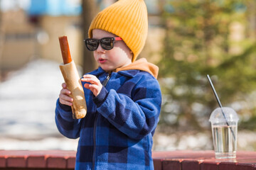 A little boy eats fast food outside in the spring. He will rub the baby in a fashionable plaid...
