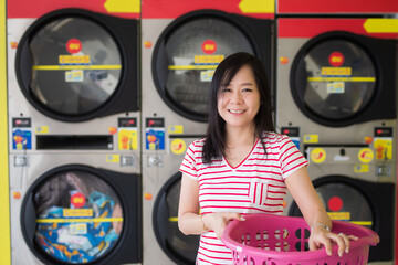 Smile asian woman holding a basket of clothes to be washed in a automatic laundry