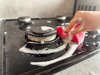 housewife cleaning dirty gas stove from grease with sponge rag in home kitchen