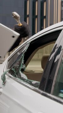 Through shattered car glass car thief stealing valuables through broken window vertical video. Car thief stealing things through broken glass testament to violated trust stolen treasures left behind.