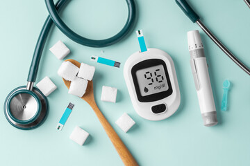 Diabetes concept with blood glucose sugar meter, sugar cubes in spoon and stethoscope on green...