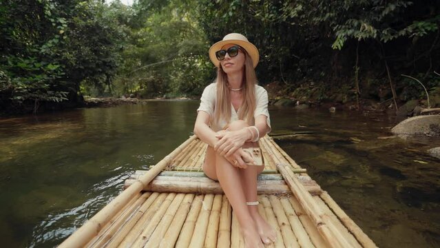 Female tourist floats on bamboo raft. Woman tourist enjoying the bamboo rafting on the river, films beautiful nature landscape wood on smartphone. Vacation, tourism, travel, adventure concept.